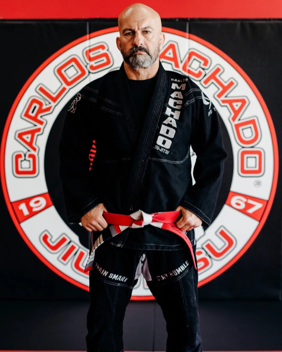 Carlos Machado in a black gi, tying his belt.